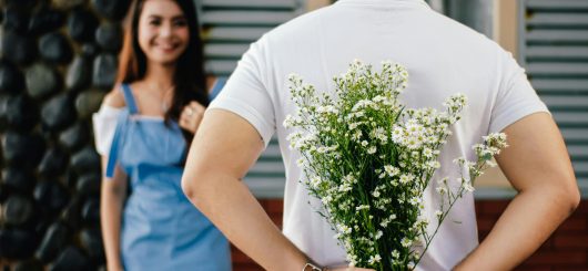 A boy holding flowers and handing them to a girl.
